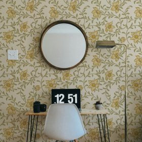 Room interior with floral wallpaper, round mirror, desk, chair, and digital clock.